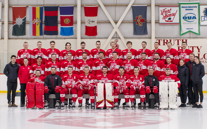 Three rows of men's hockey players with support staff on the side and coaches and captains in the front row.